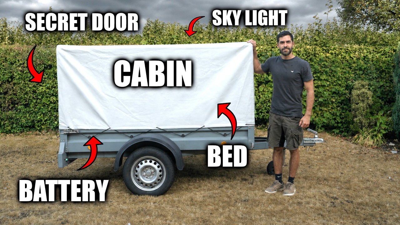 A man building a rustic wooden cabin inside a small trailer with a corrugated plastic roof and acrylic windows.